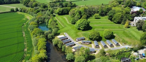 An aerial view of a rural property with a river, green fields, and a row of cabins.