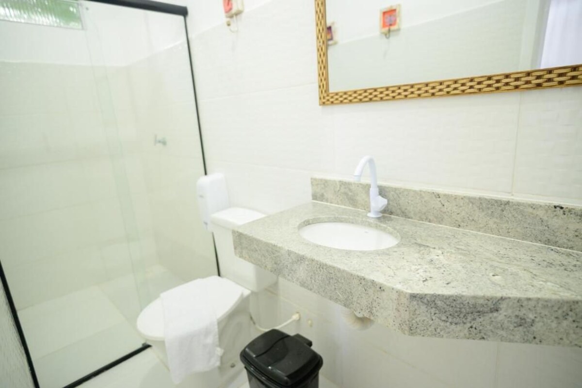 Une salle de bain avec une douche à parois de verre, des toilettes blanches, un lavabo en granit avec un robinet blanc et une poubelle noire.