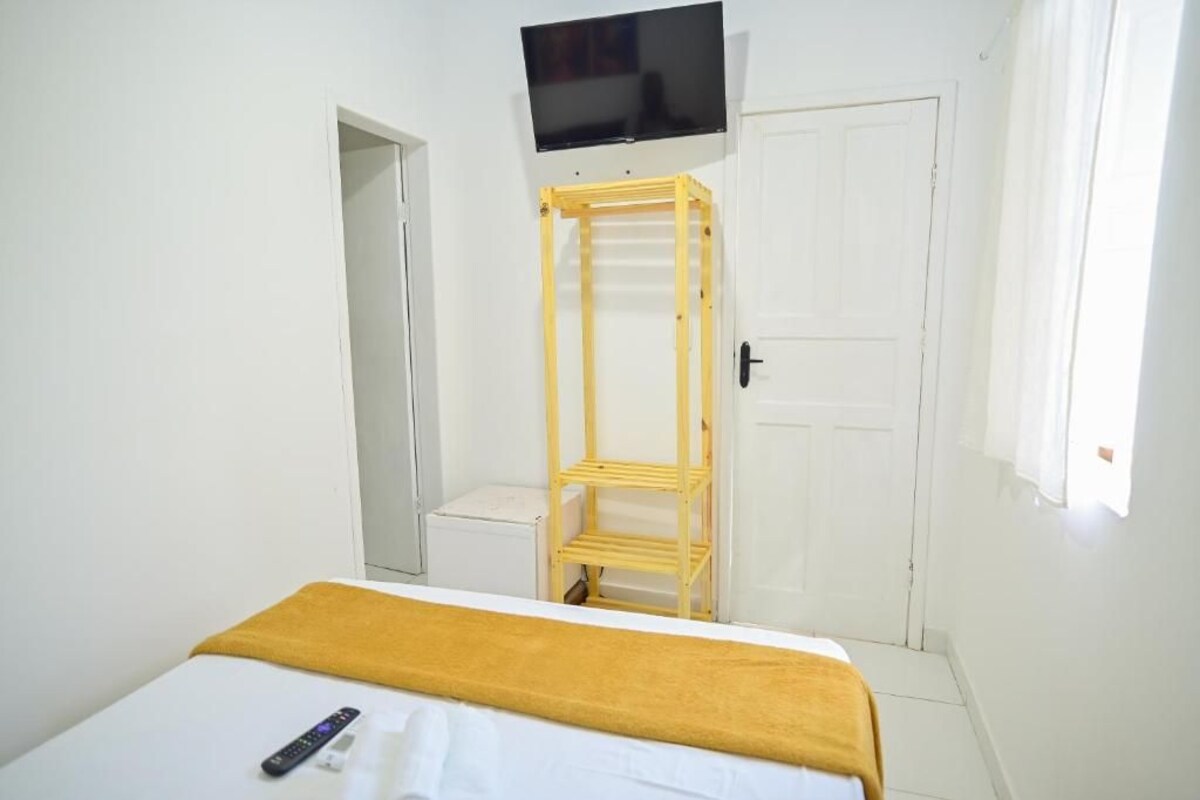 Un dormitorio con cama, televisión montada en la pared, escalera de madera y puerta blanca.