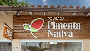 En butik med facade af træ og et stort glasvindue. Skiltet viser "POUSADA Pimenta Nativa" og inkluderer et telefonnummer.