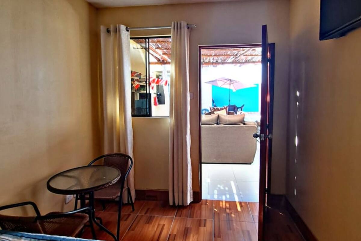 A hotel room with a bed, a small table, and a chair. There is a door leading to a balcony with a view of the outside.