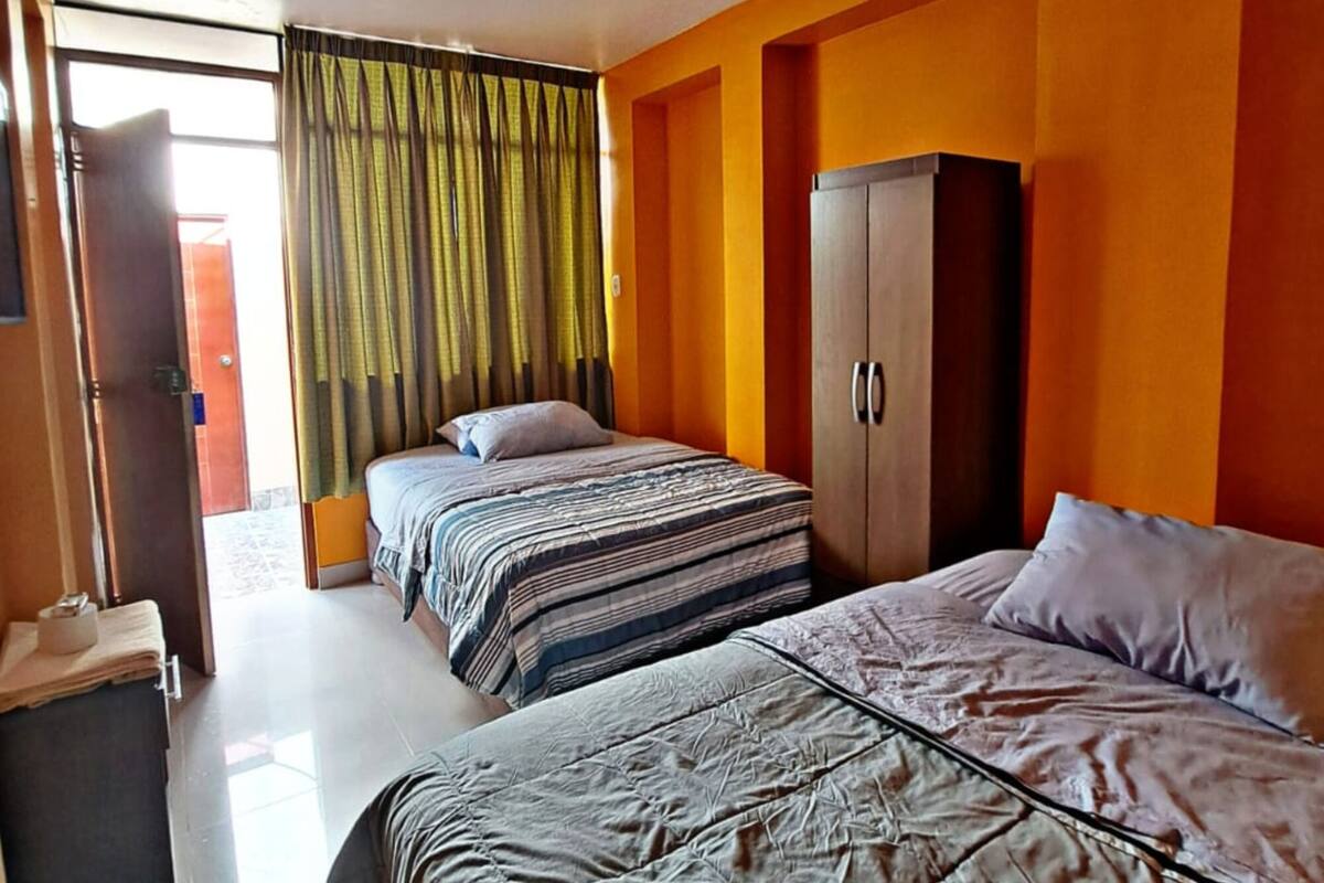A hotel room with two beds, a wardrobe, a ceiling fan, and a view of the outside.