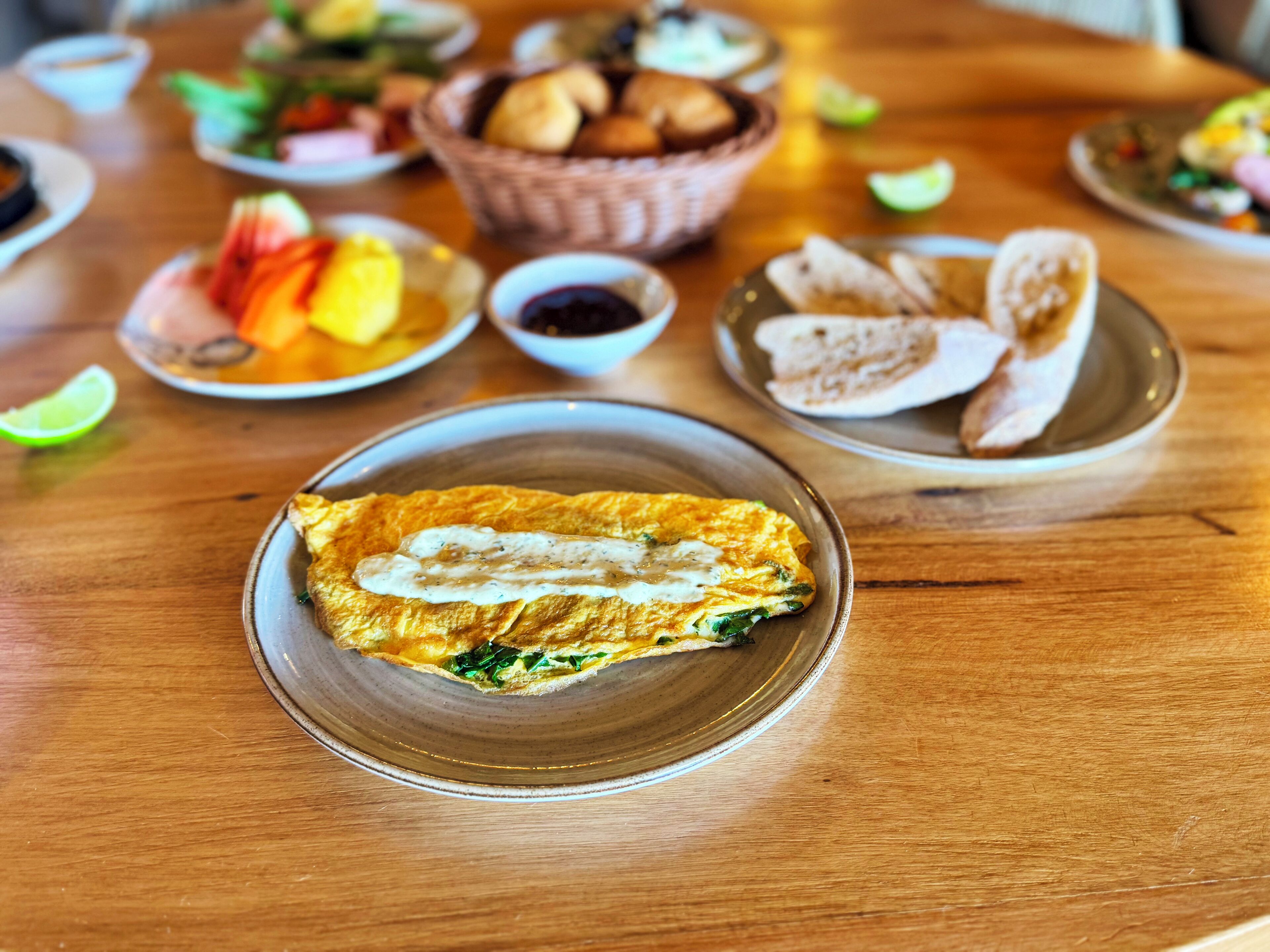 A table with various dishes including a plate of omelette, bowls of fruit, and bread.