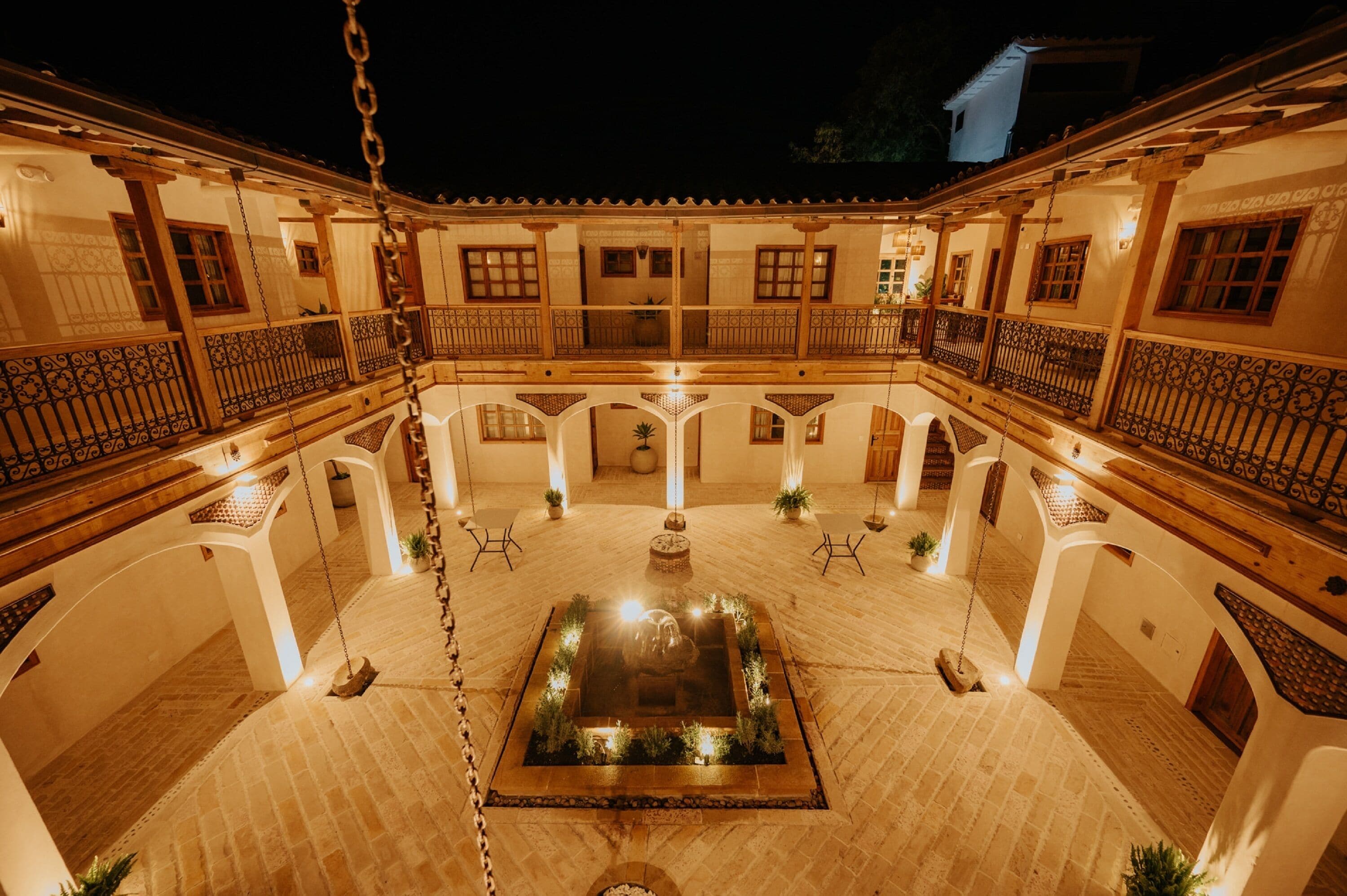 A courtyard with a central fountain, surrounded by white walls and wooden balconies with wrought iron railings.