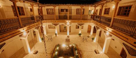 A courtyard with a central fountain, surrounded by white walls and wooden balconies with wrought iron railings.