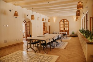 Una amplia sala de conferencias con largas mesas y sillas, pisos de madera y lámparas colgantes.