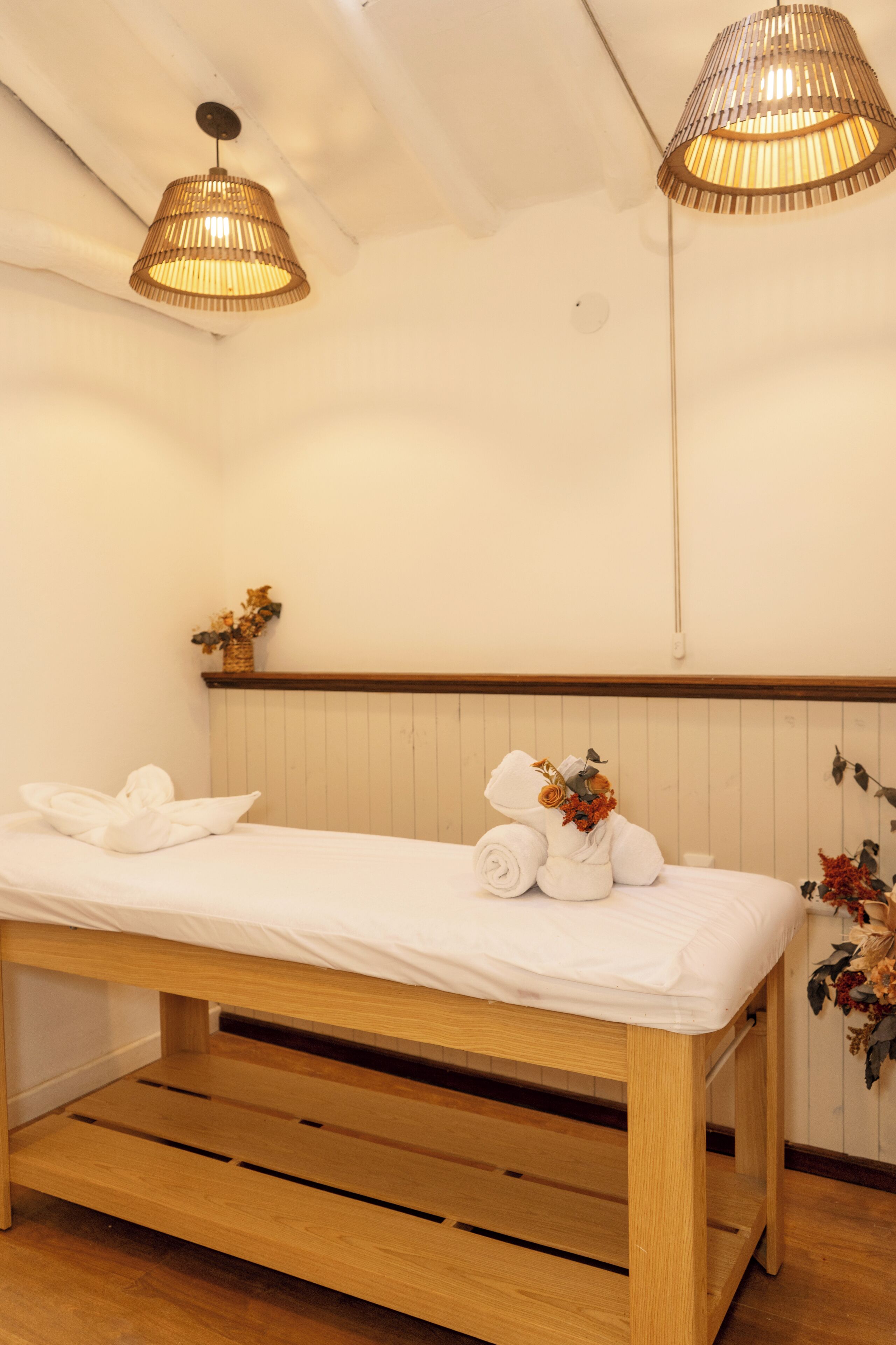 A single bed with a wooden frame and white bedding, a small bedside table, and two hanging lamps.