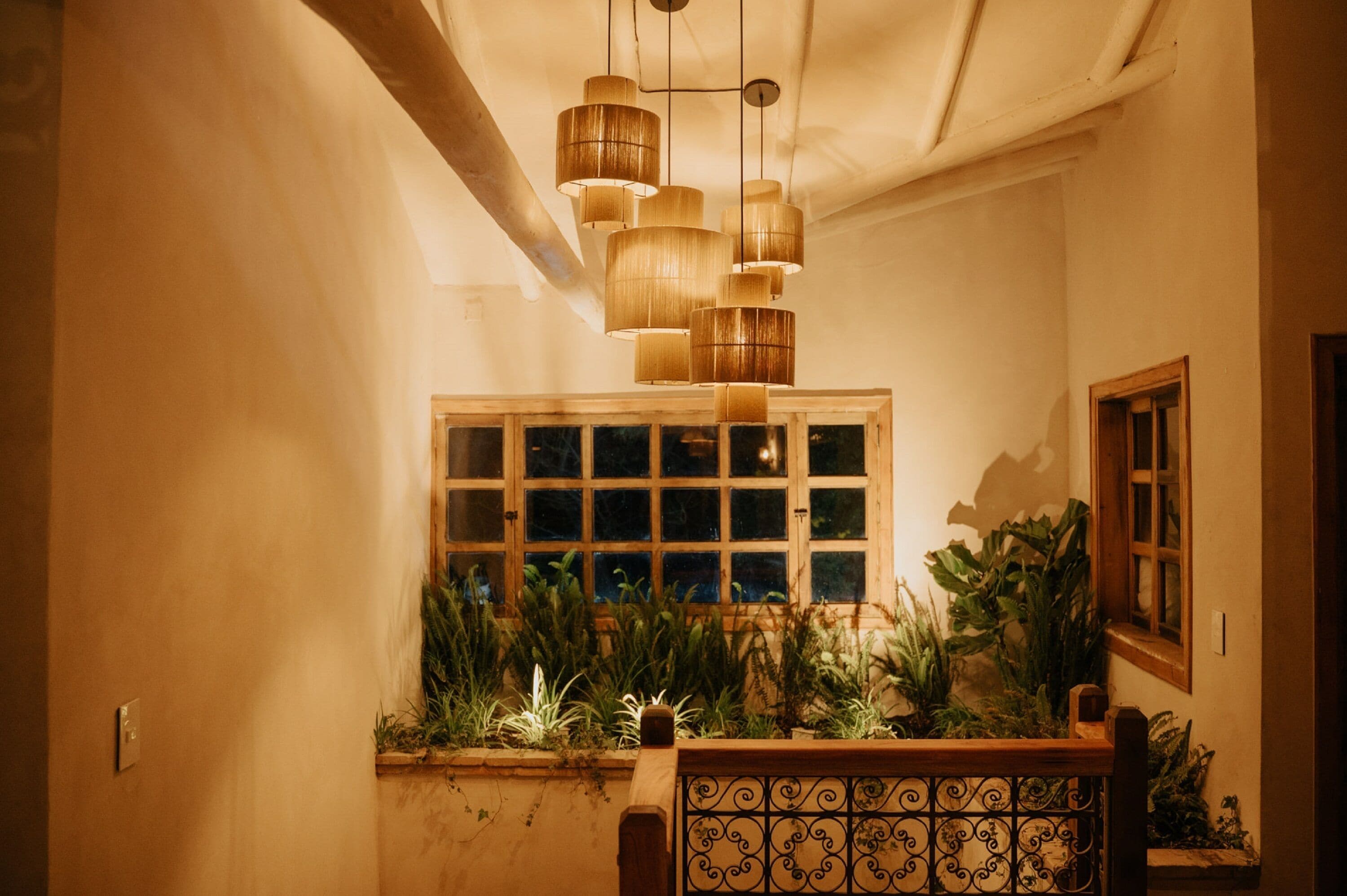 Un pasillo con un banco de madera, una ventana con plantas y un candelabro colgante.