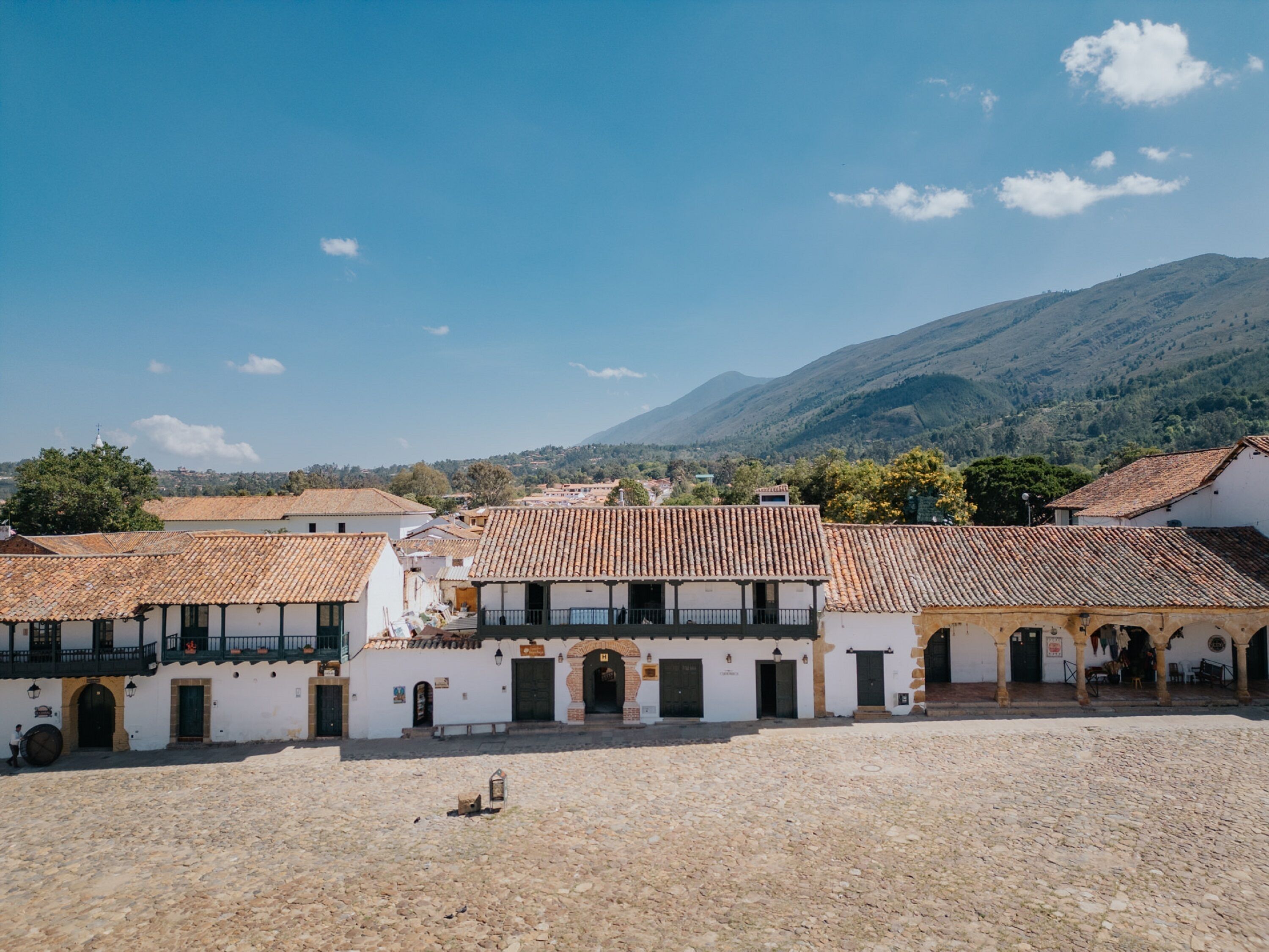 A courtyard with traditional buildings, stone flooring, and a mountainous backdrop.