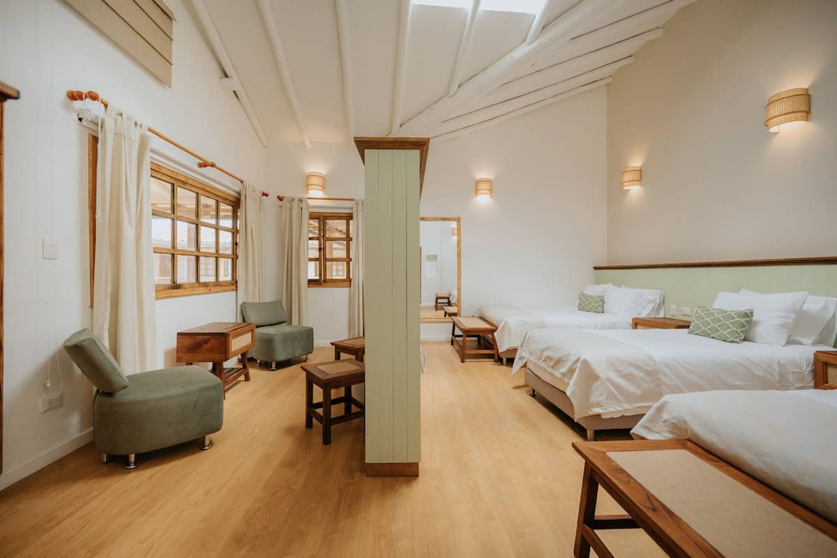 A hotel room with wooden floors, two single beds, a sofa, a small table, and a window with curtains.