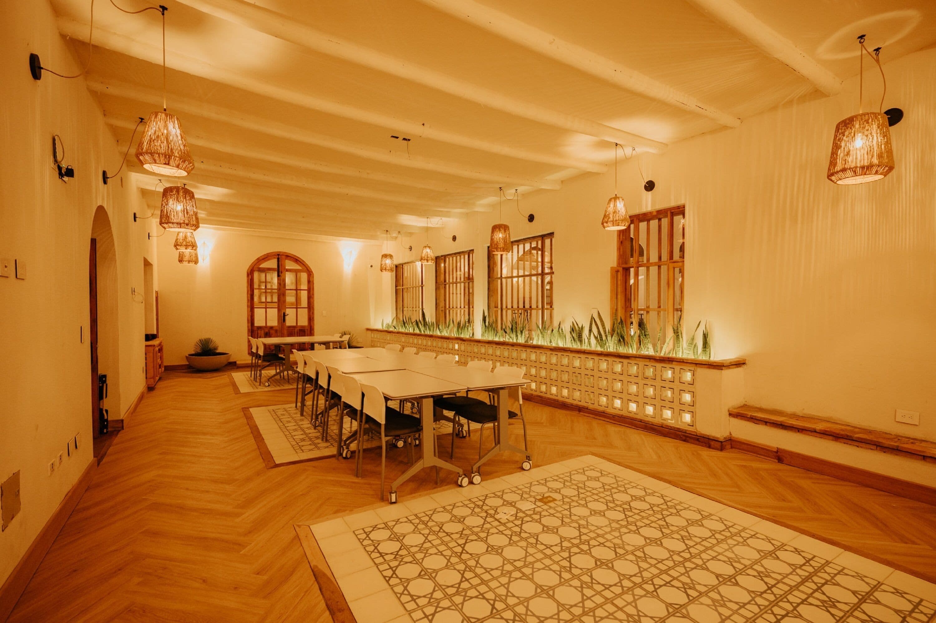 A spacious room with a long table, multiple chairs, and hanging lamps.