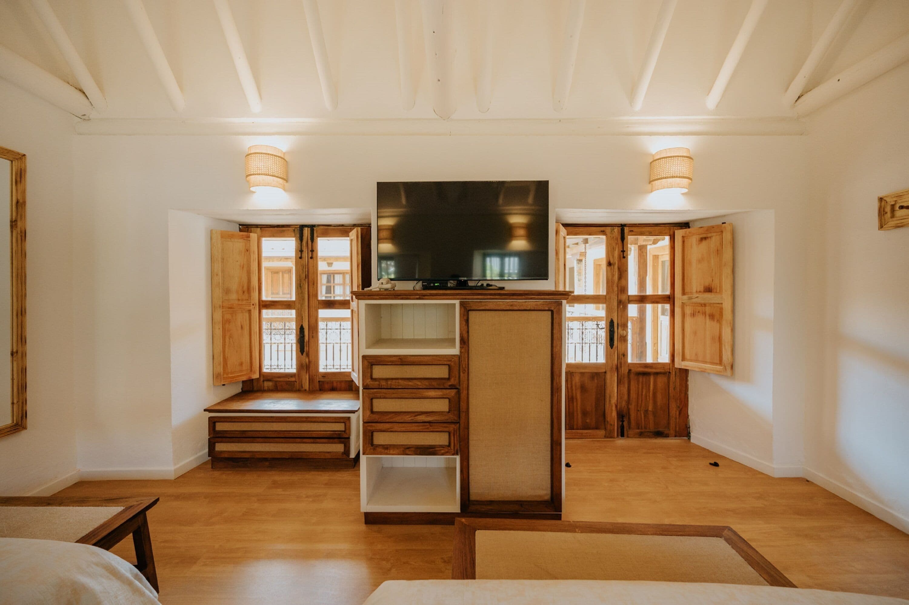 A spacious living room with a large flat-screen TV mounted on a wooden stand, flanked by two wooden cabinets and a bench.