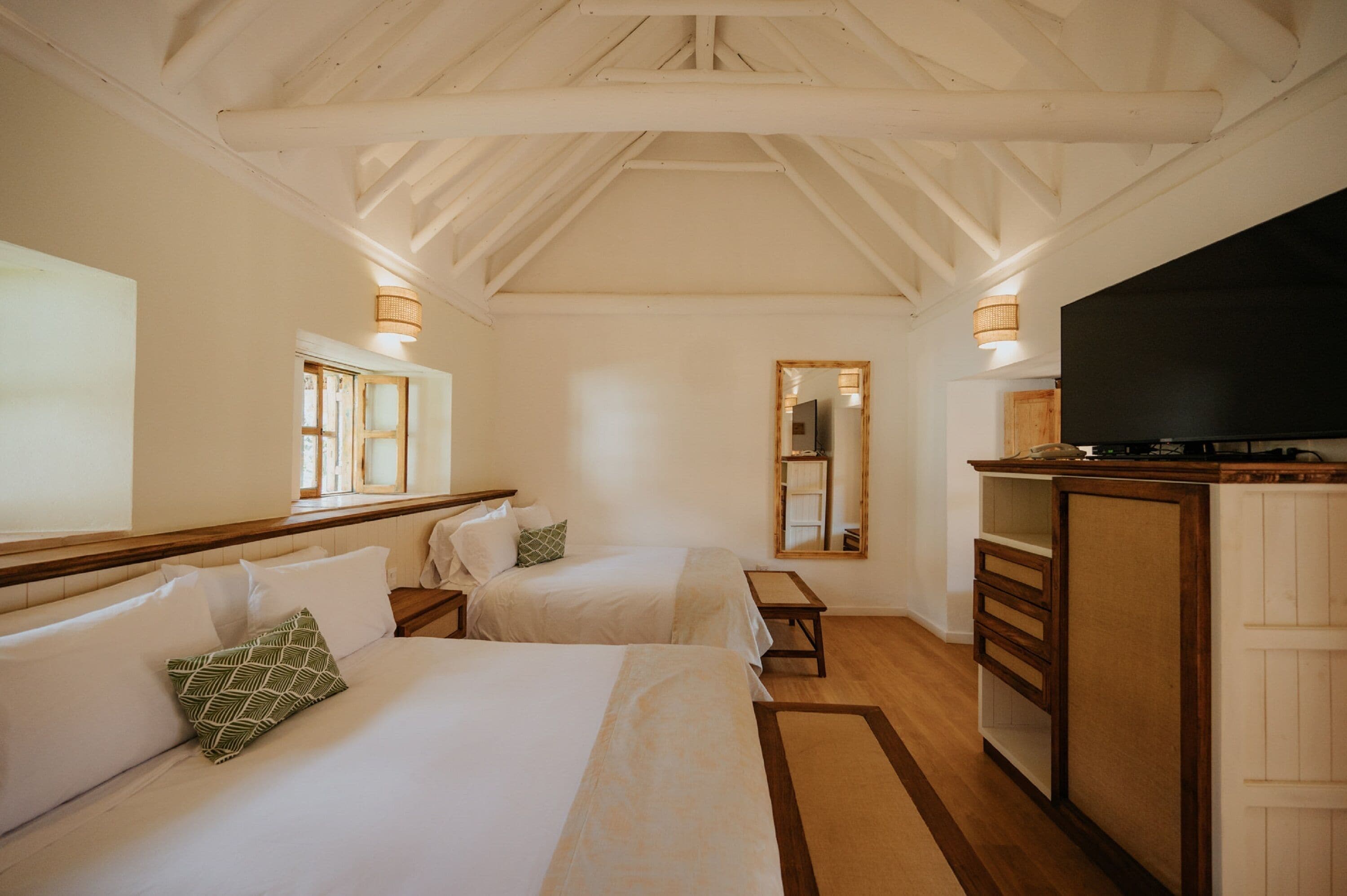 A hotel room with two beds, a TV, wooden furniture, and a mirror.