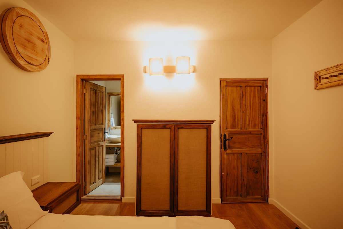 A bedroom with a bed, wooden wardrobe, and a wall-mounted light fixture.