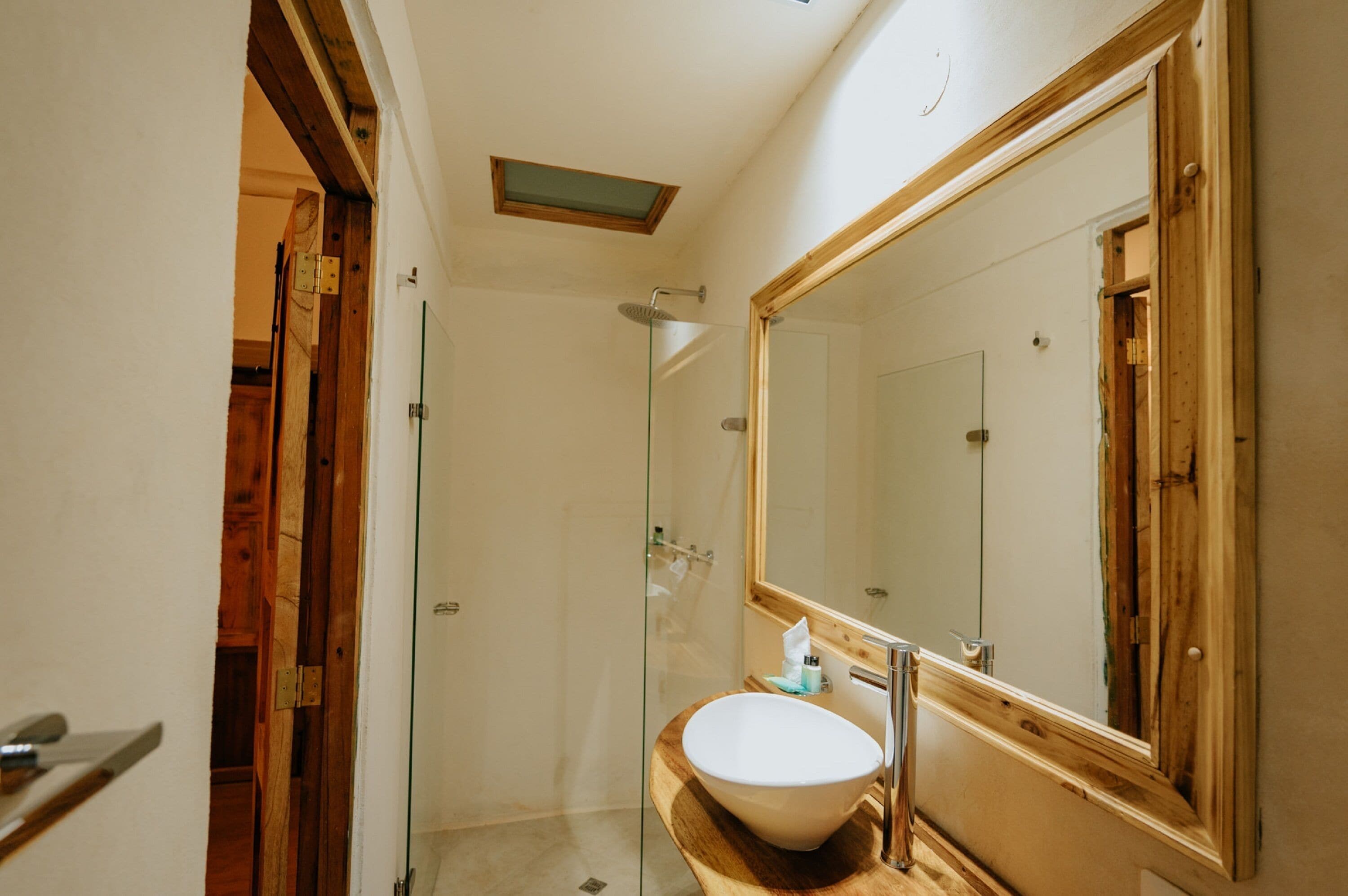 Une salle de bain avec un meuble-lavabo en bois, un grand miroir et une cabine de douche en verre.