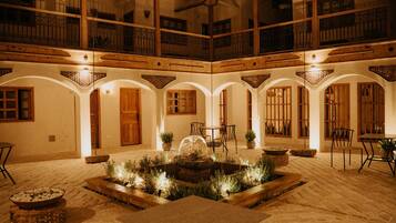 A courtyard with a fountain, wooden furniture, and a balcony.