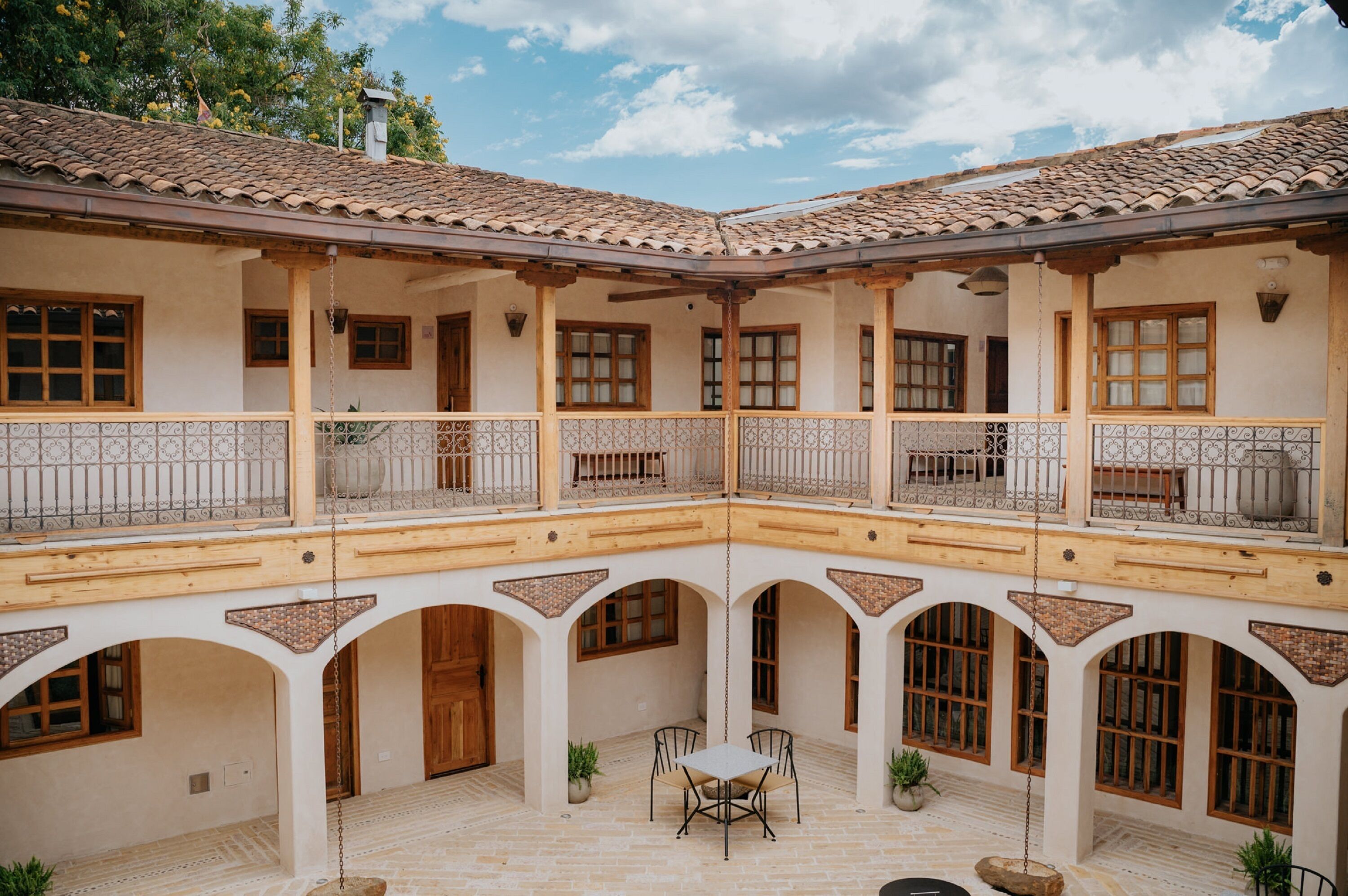 A courtyard with a central table and chairs, surrounded by arches and balconies with wooden railings.