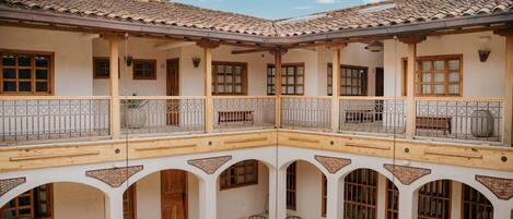 A courtyard with a central table and chairs, surrounded by arches and balconies with wooden railings.