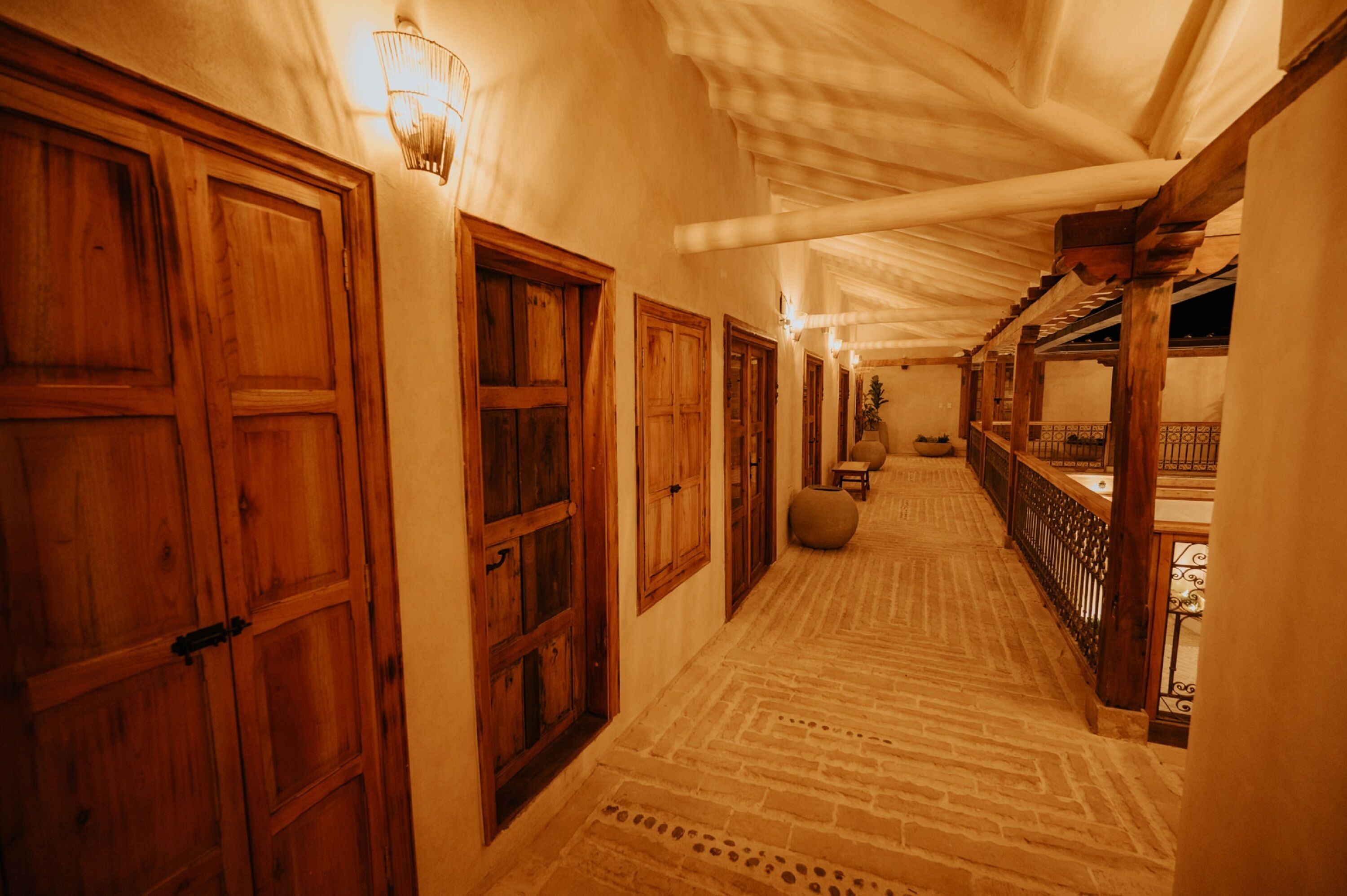 A corridor with wooden doors and a patterned floor, leading to a balcony with a railing.