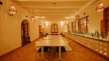 Un salón de conferencias con una larga mesa, pisos de madera y lámparas colgantes.