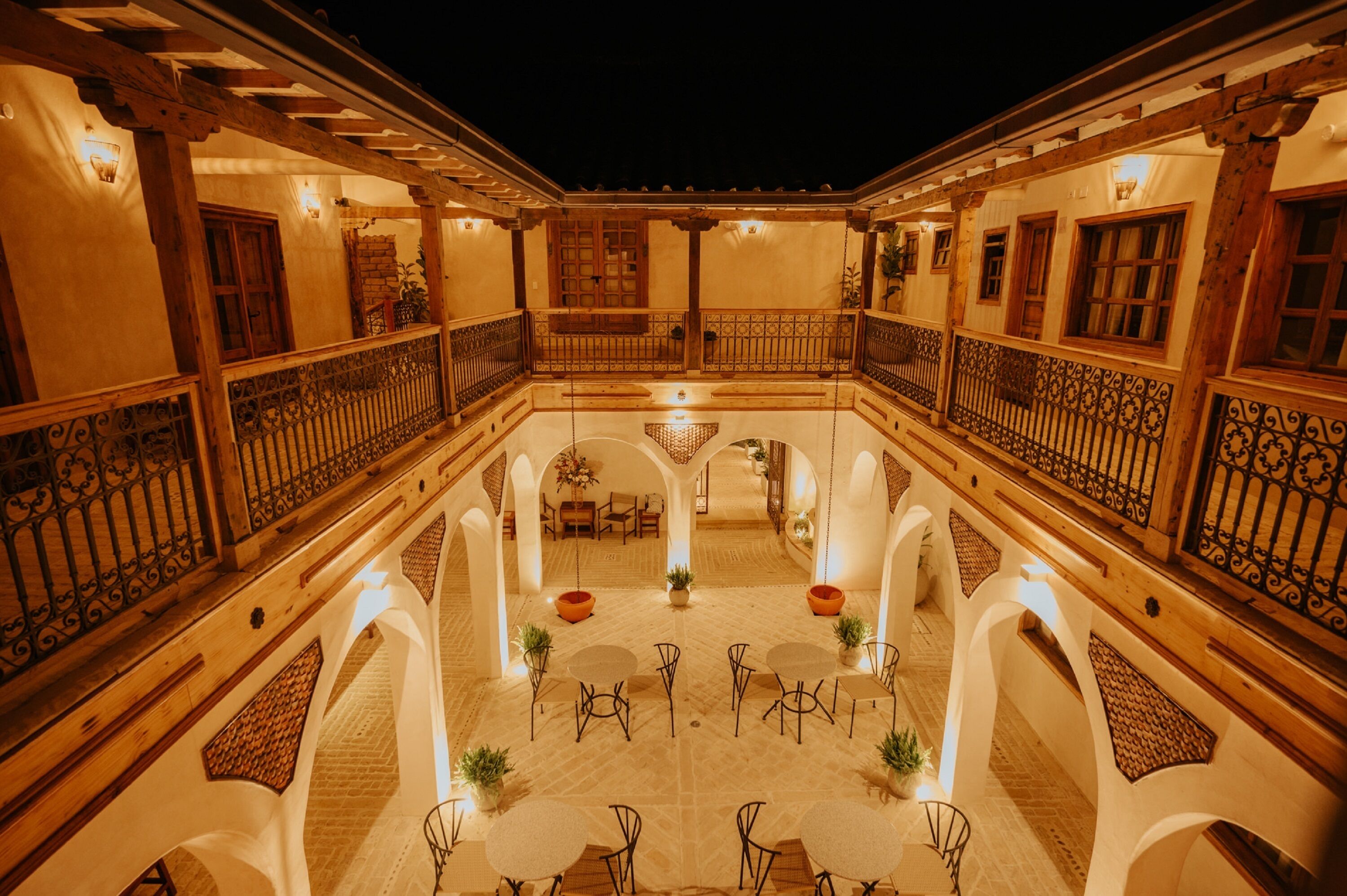 A courtyard with a central seating area, surrounded by white walls and wooden beams, featuring tables and chairs.