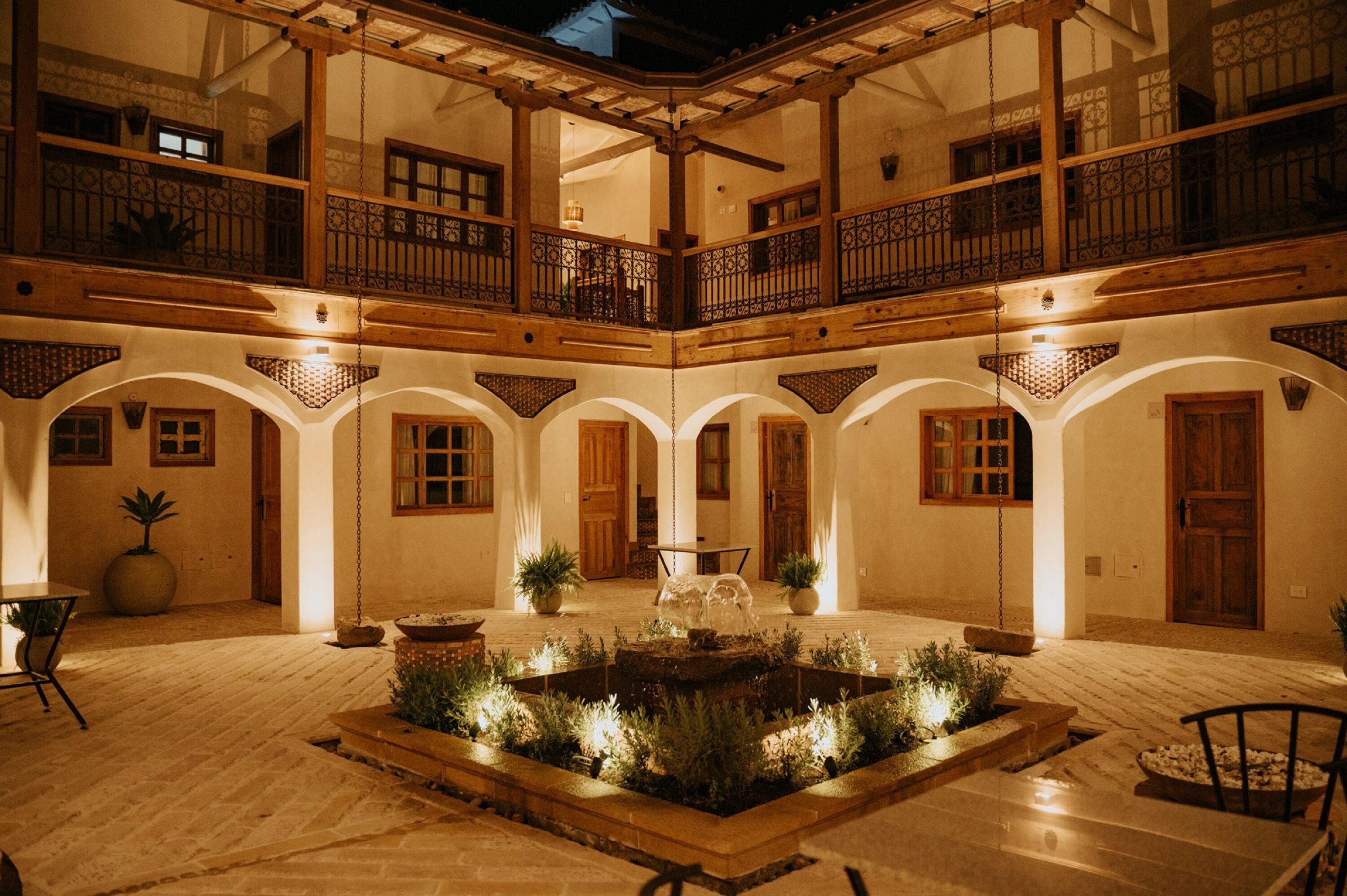 A courtyard with a fountain, wooden furniture, and potted plants.