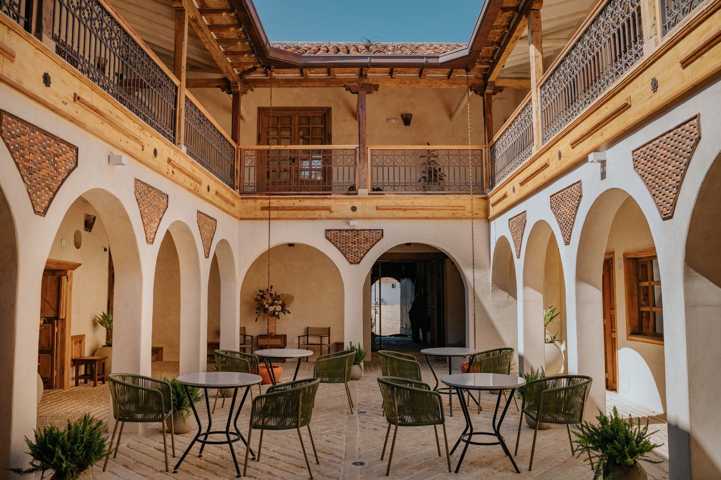 Un patio con varias mesas y sillas, vigas de madera y arcos.