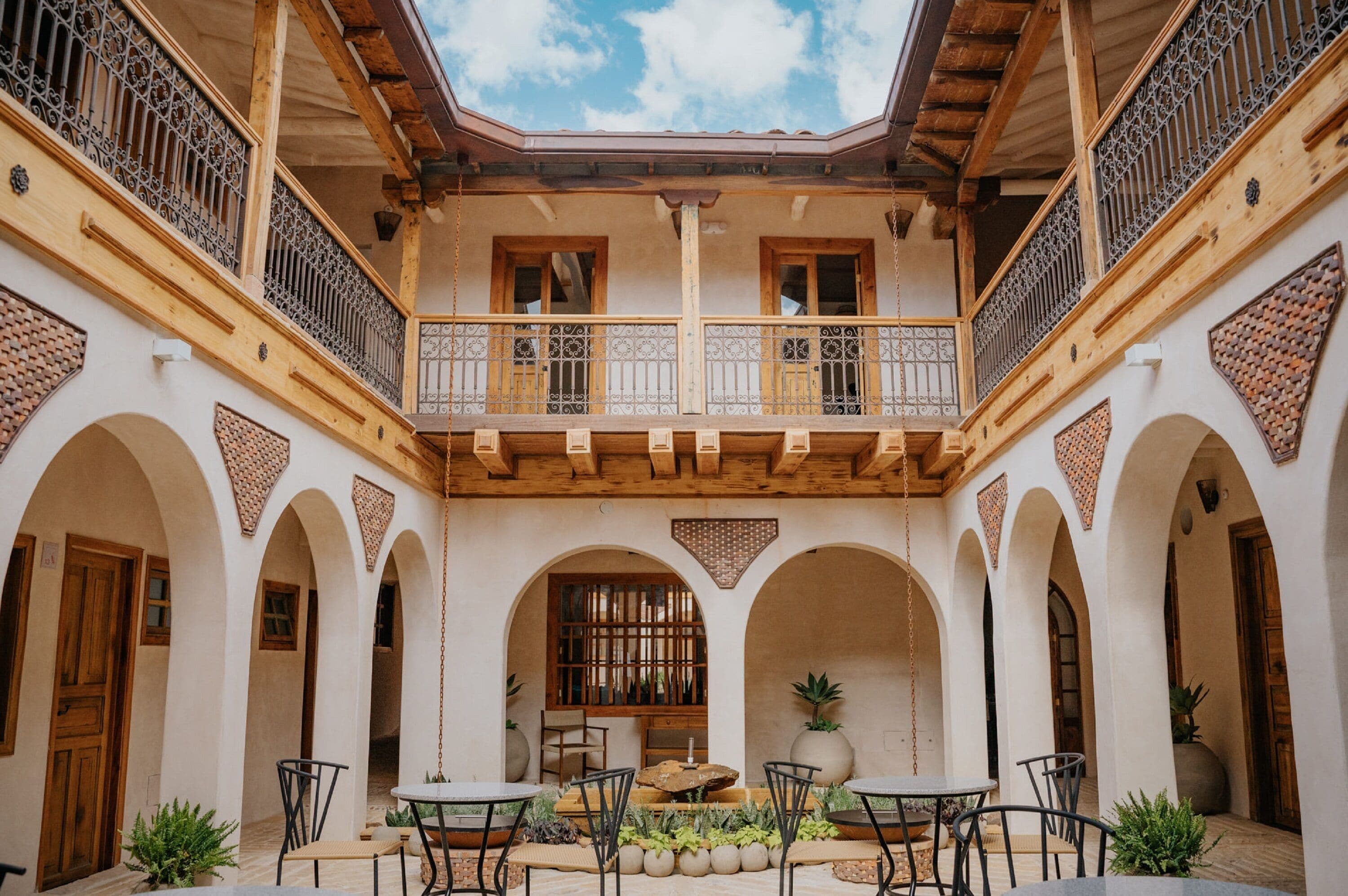 A courtyard with a central seating area, wooden balconies, and arched doorways.