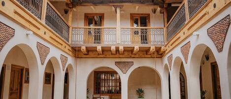 A courtyard with a central seating area, wooden balconies, and arched doorways.
