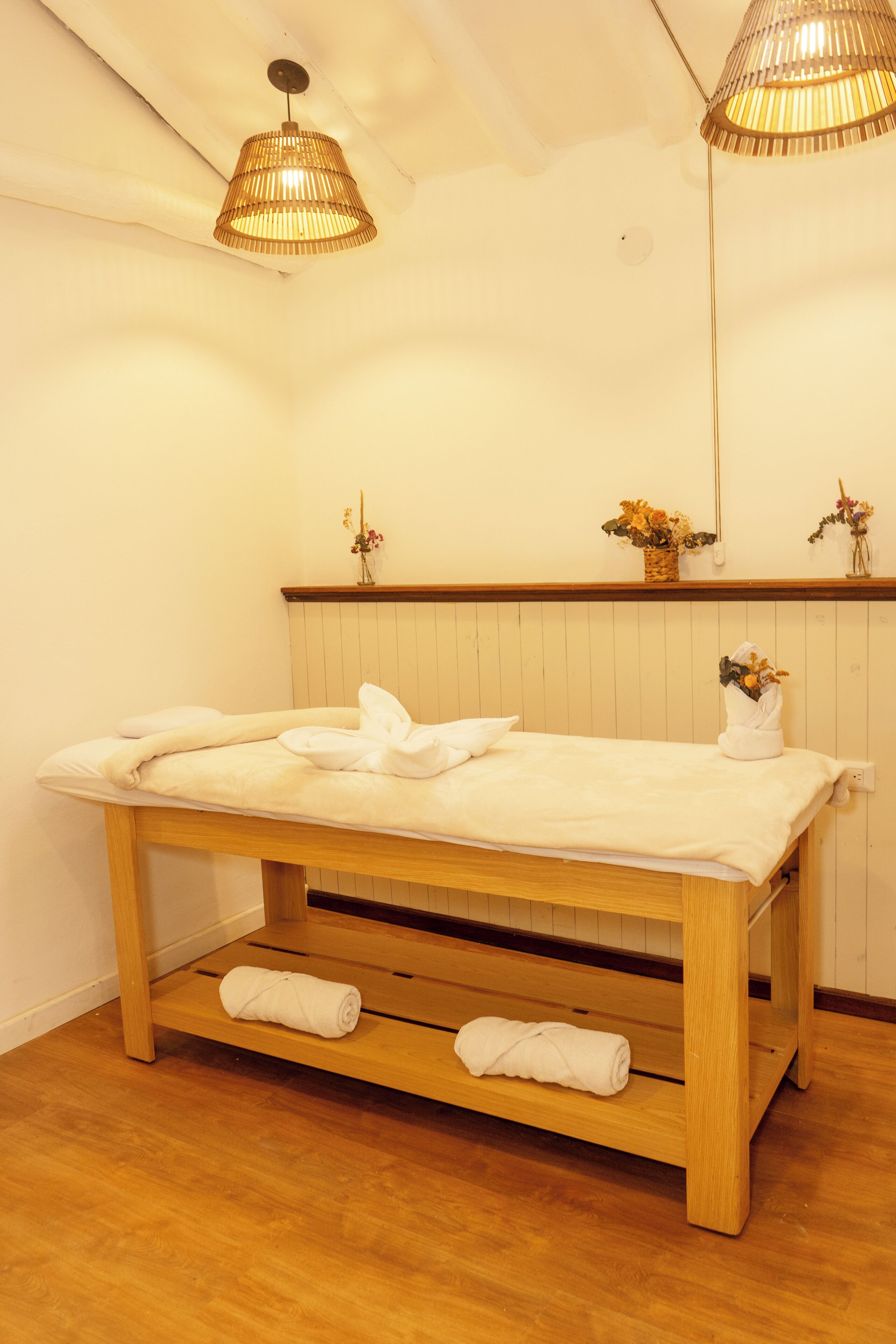 A wooden massage table with towels, a wooden bench, and a ceiling light fixture.