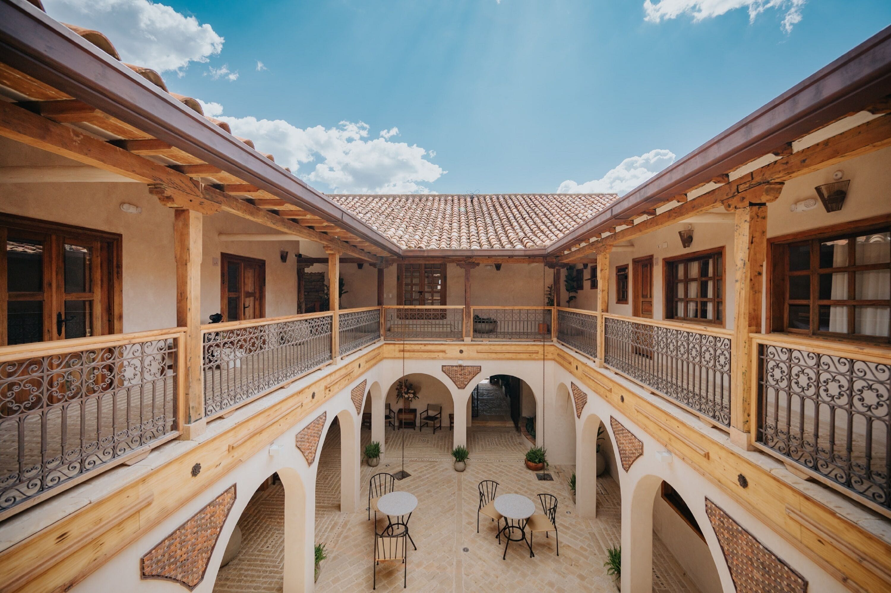 Un patio con techo de tejas, vigas de madera y una zona de estar central con mesas y sillas.