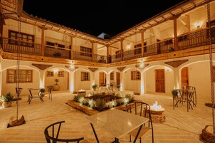 Un patio con una fuente central, rodeado de mesas y sillas, y varios balcones con barandas de madera.