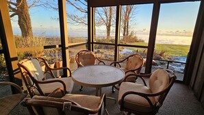 A covered outdoor seating area with wicker furniture and a glass table, overlooking a snowy landscape and trees.