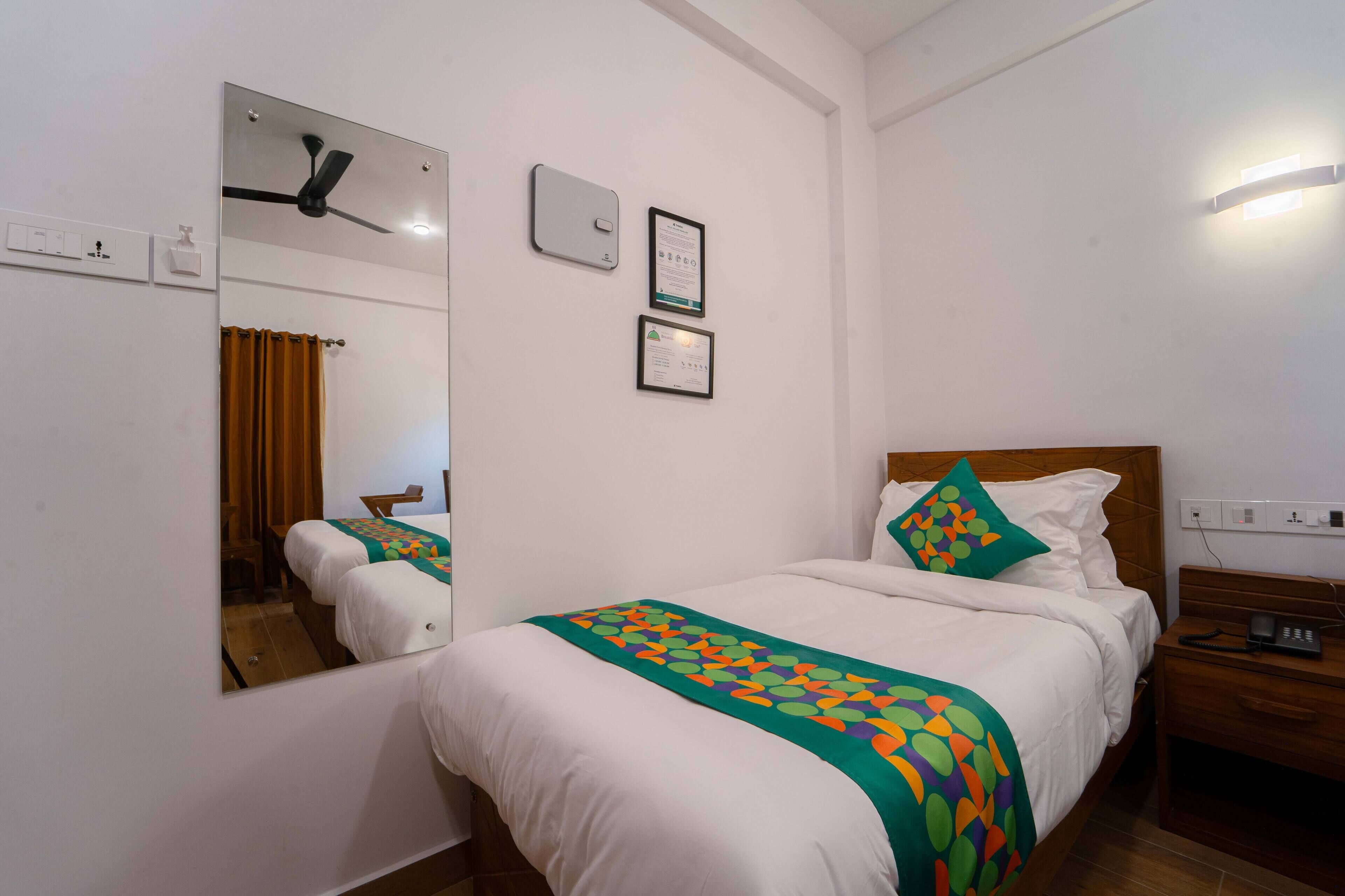 Habitación de hotel con cama, mesita de noche, espejo y ventilador de techo.
