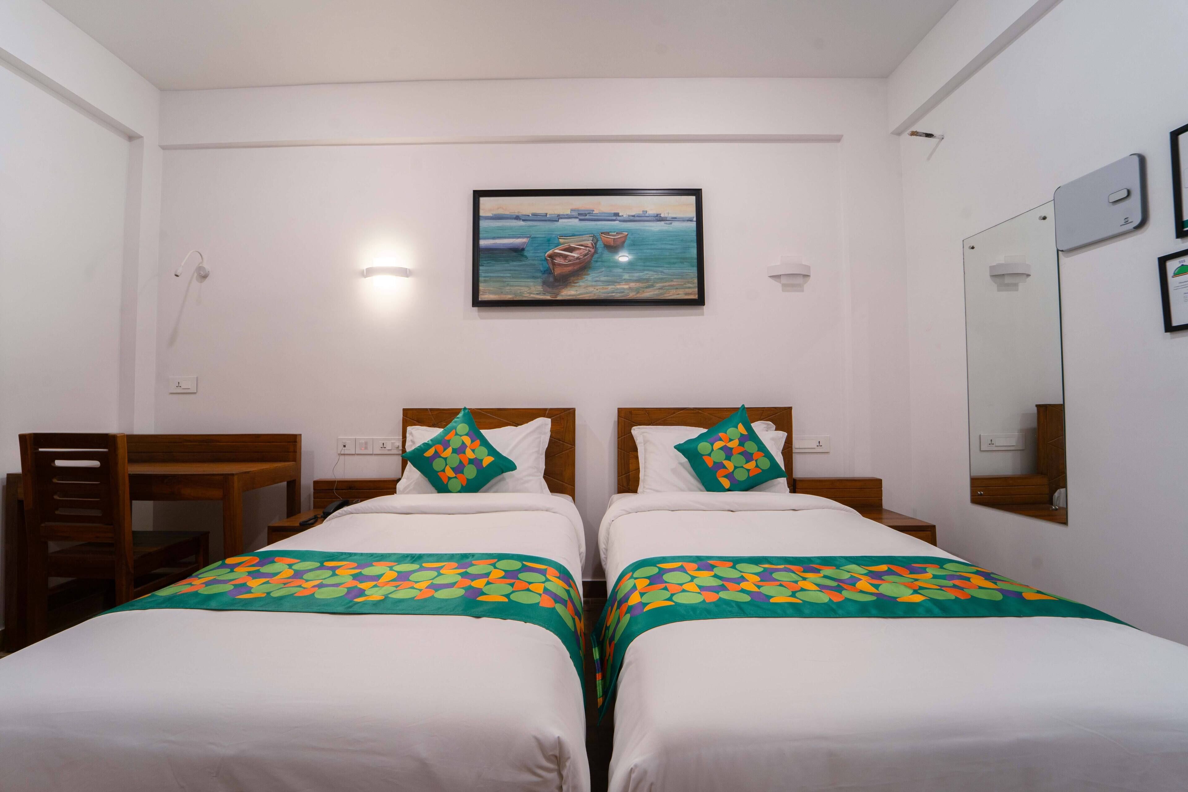 Une chambre d’hôtel avec deux lits simples, un bureau, une chaise, un tableau au mur et un miroir.