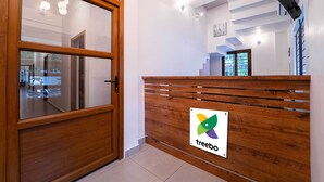 A reception area with a wooden reception desk, a logo, and a ceiling fan. - Treebo West Fort Divine – Near Padmanabhaswamy Temple (Thiruvananthapuram)