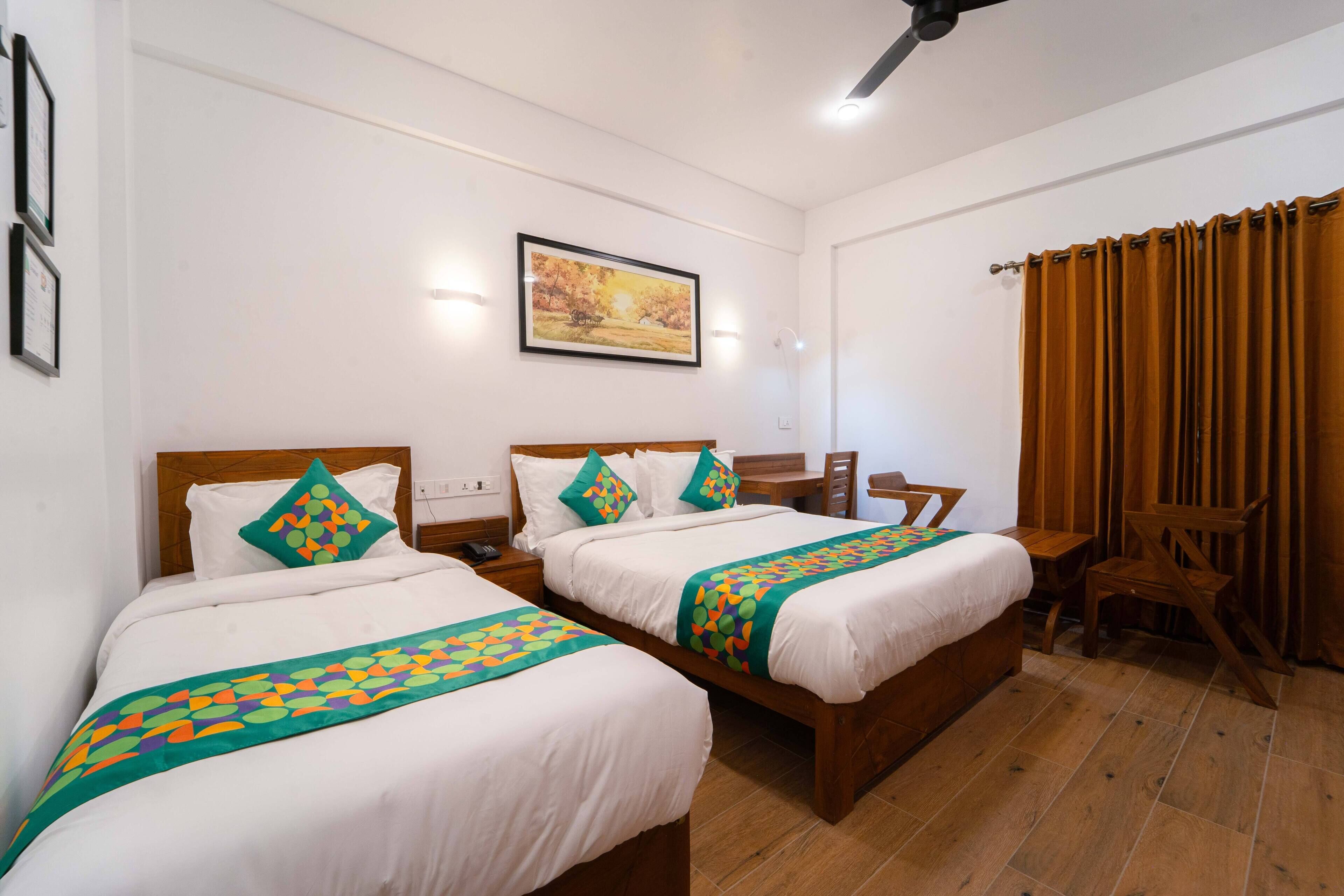 Quarto de hotel com duas camas, uma escrivaninha, uma cadeira e um quadro na parede.