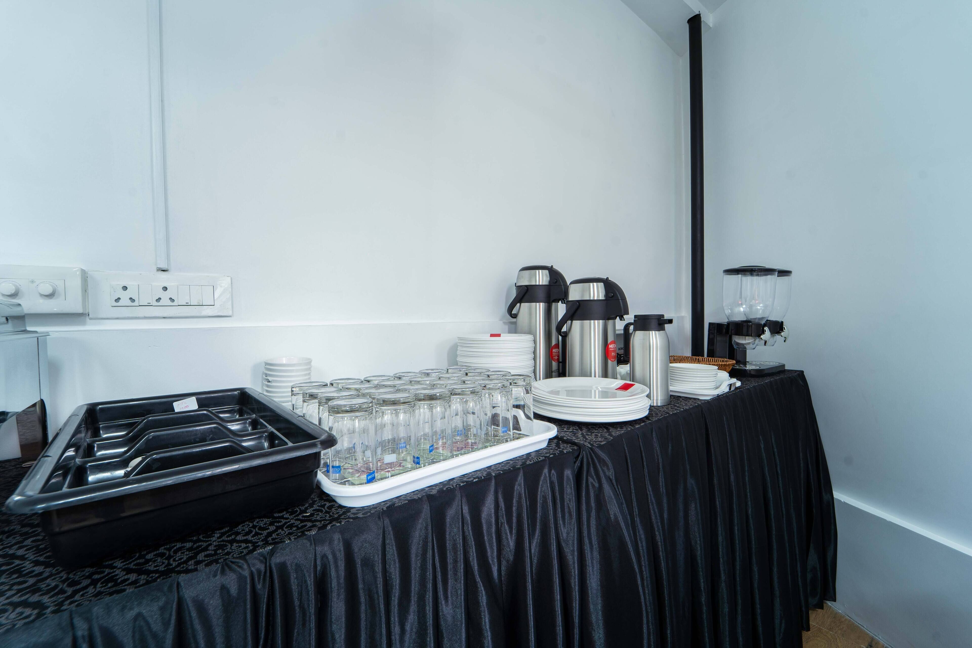 A buffet setup with a black tablecloth, glassware, plates, and coffee makers.