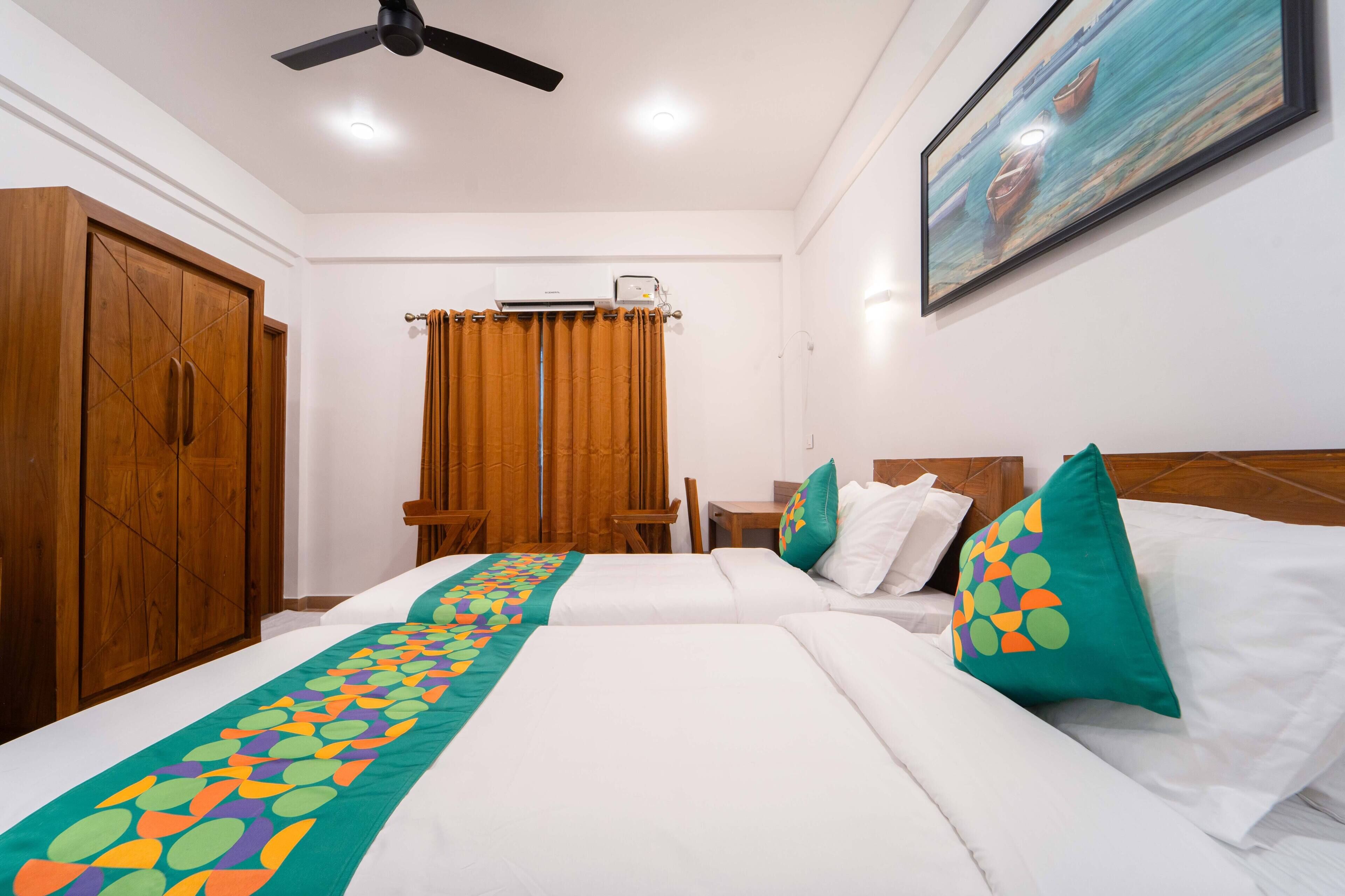 A hotel room with two beds, a wooden wardrobe, a ceiling fan, an air conditioning unit, a painting on the wall, and a window with curtains.