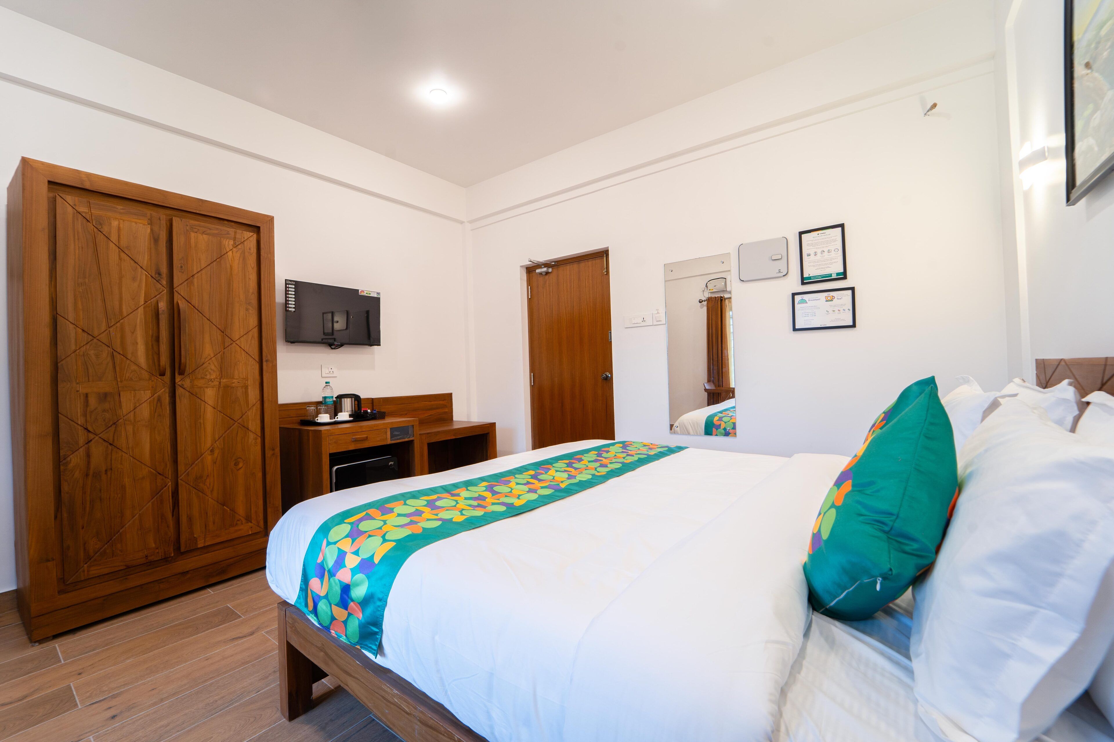 A hotel room with a large bed, wooden wardrobe, desk, and a television on the wall.