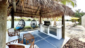 Une terrasse extérieure dotée d’un toit de chaume, d’un barbecue, de sièges et offrant une vue sur une étendue d’eau.