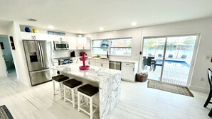 Une cuisine moderne dotée d’un îlot central, de tabourets de bar et offrant une vue sur la piscine grâce à de grandes portes-fenêtres coulissantes.