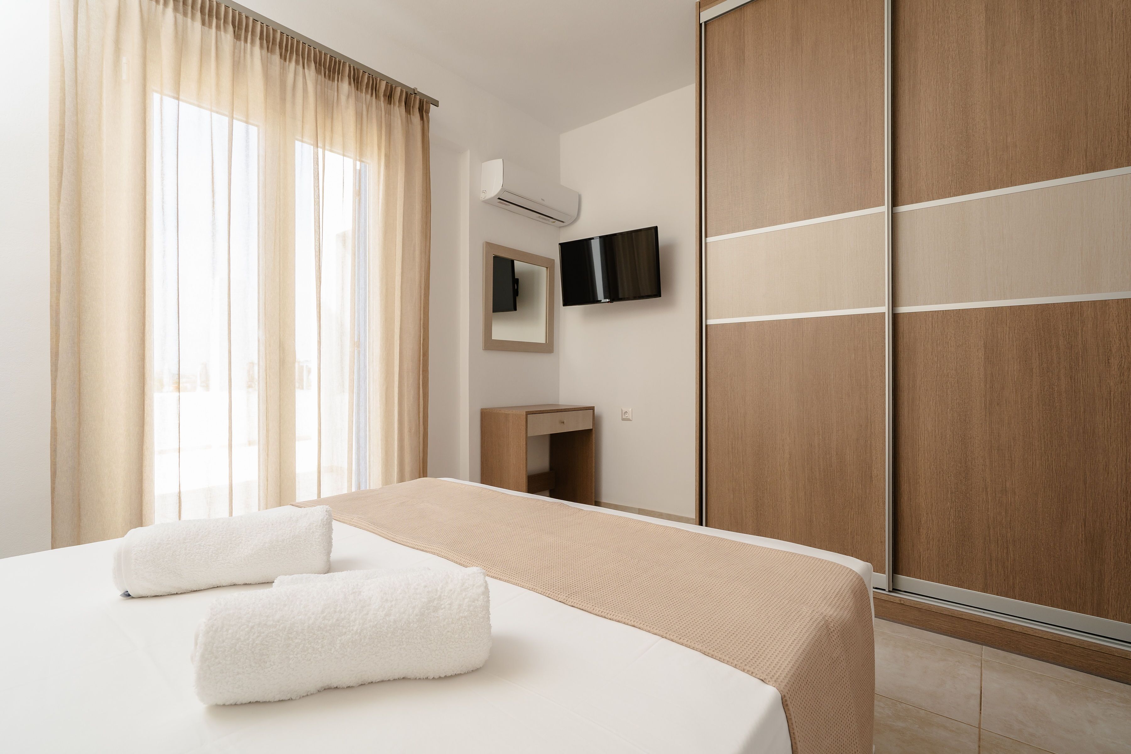 Een hotelkamer met een bed, een televisie, een spiegel, een kledingkast en een raam met gordijnen.