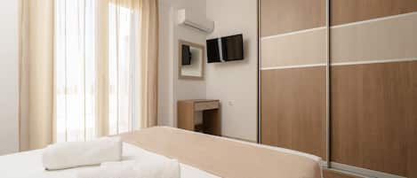 Een hotelkamer met een bed, een televisie, een spiegel, een kledingkast en een raam met gordijnen.
