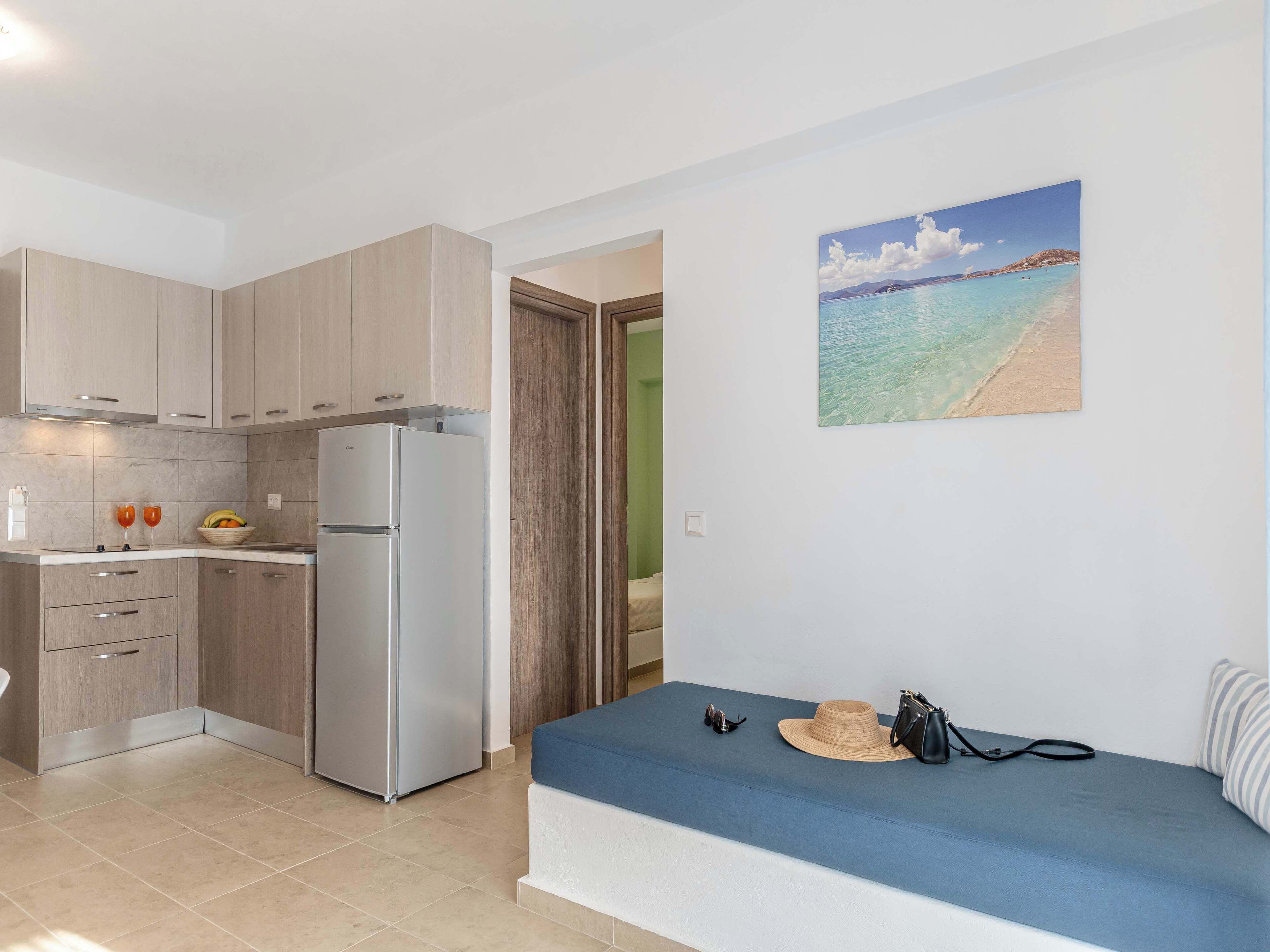 A modern kitchen with light wood cabinets, a stainless steel refrigerator, and a dining area with a blue bench.
