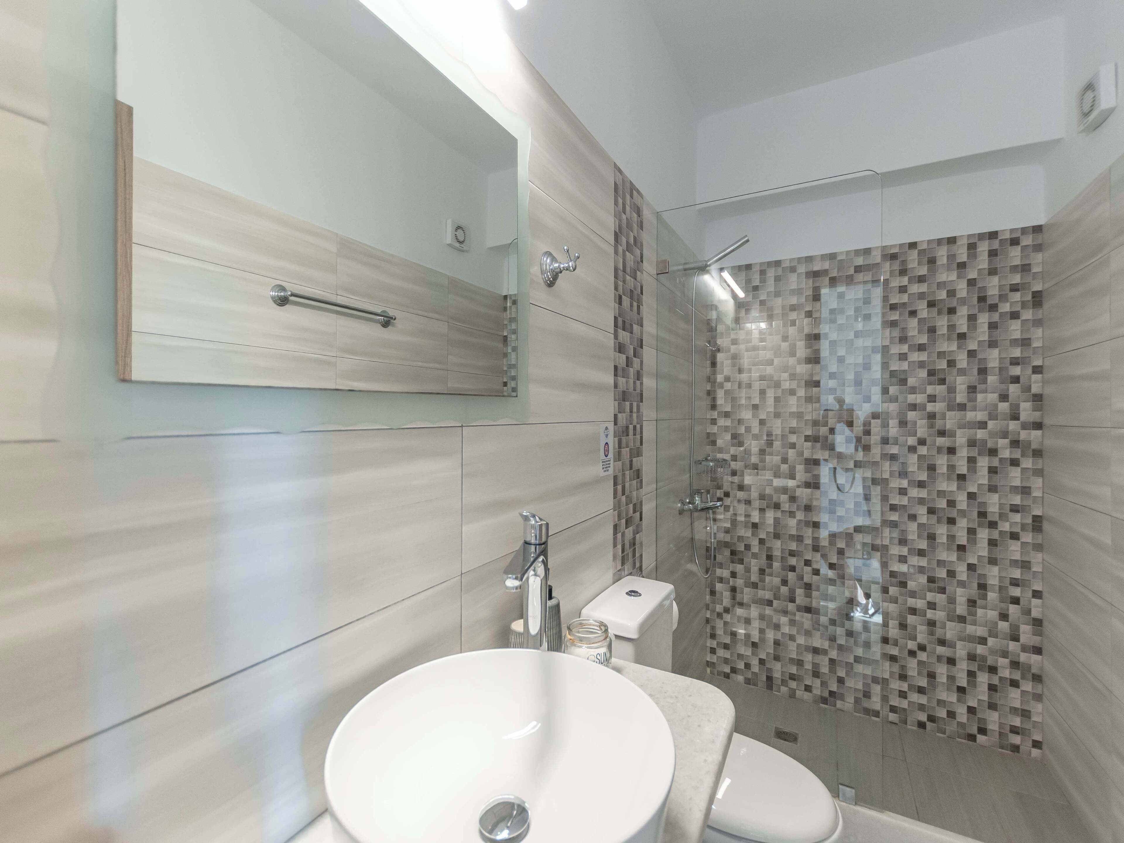 Une salle de bain moderne avec un grand miroir, un lavabo, des toilettes et un espace douche aux murs recouverts de mosaïques.