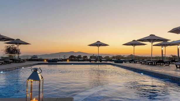 Una piscina con sillas de descanso y sombrillas, rodeada de montañas.