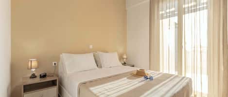 A hotel room with a bed, bedside tables, a lamp, and a window with curtains.