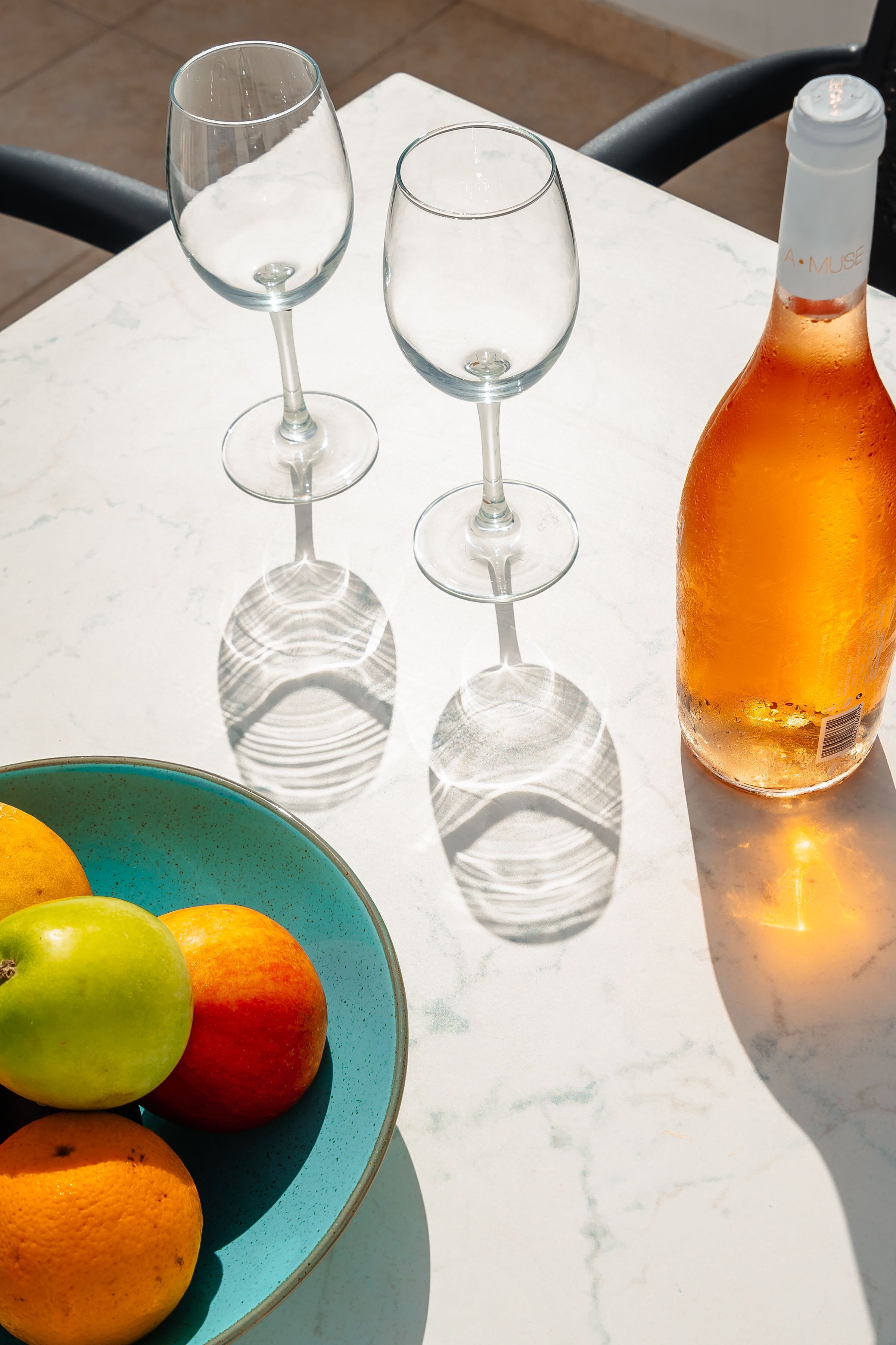 A table with three wine glasses, a bottle of wine, and a bowl of fruit.