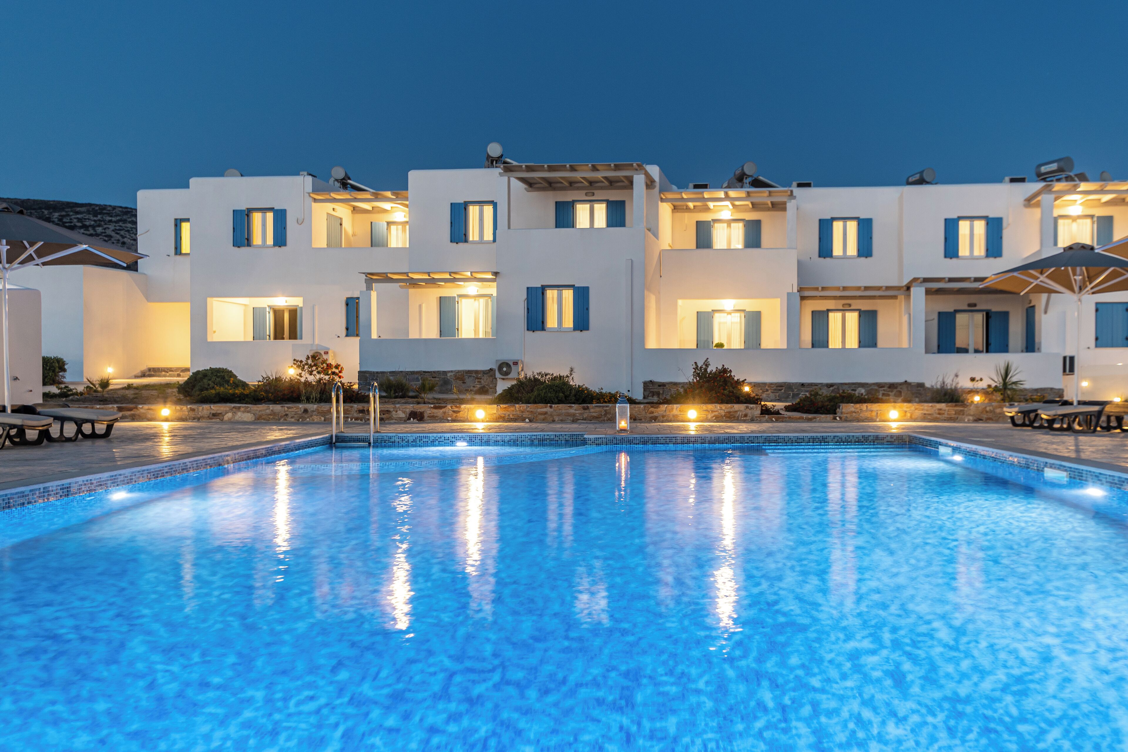 A swimming pool with a clear blue water surface, surrounded by a building with multiple balconies and windows.